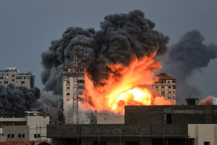Un grupo de personas en una azotea observa cómo una bola de fuego y humo se eleva sobre un edificio en la ciudad de Gaza.
