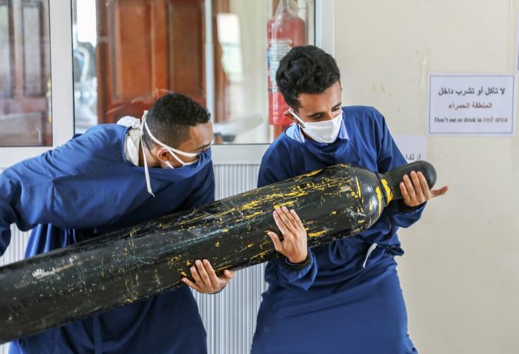 Dos trabajadores del centro Al-Sahul de COVID-19 están tratando de trasladar una botella de oxígeno al interior de la Unidad de Cuidados Intensivos. 