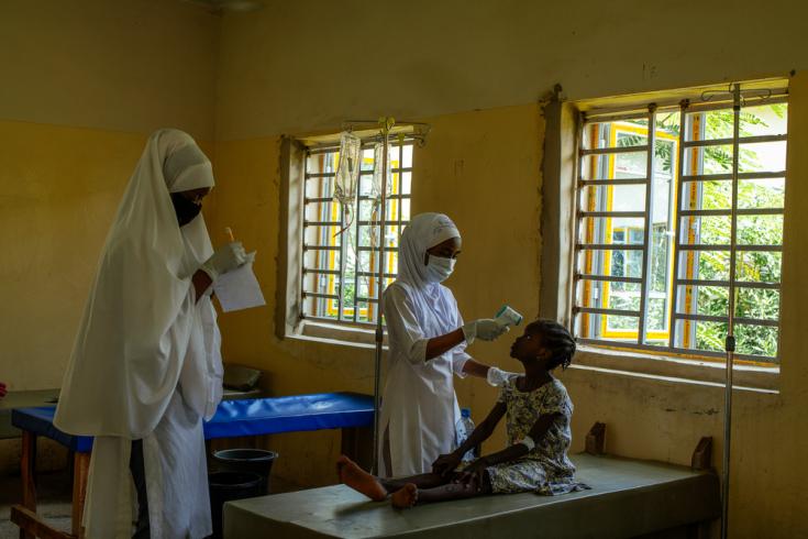 Una enfermera de nuestros centros de tratamiento para el cólera en Kano verifica la temperatura corporal de una paciente usando el termómetro infrarrojo mientras otra enfermera hace un registro escrito del análisis.