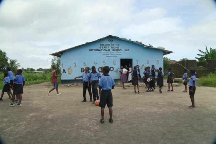 Niños y niñas de uniforme jugando a la pelota y a saltar la soga frente a escuela