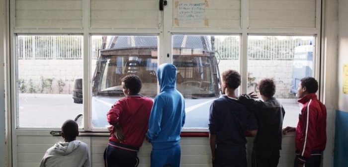 Un grupo de jóvenes provenientes de Eritrea miran desde la puerta del Centro de Recepción en Pozzallo, bloqueada con una camioneta para evitar que las personas escapen. ©Alessandro Penso