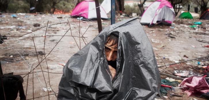 Octubre de 2015. un refugiado afgano se refugia de una tormenta con una bolsa de basura en el punto de acceso de Moria, Grecia. ©Alessandro Penso