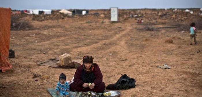 Un bebé sentado mientras su abuela pela berenjenas. Son refugiados sirios atrapados en el desierto, en la frontera con Jordania.