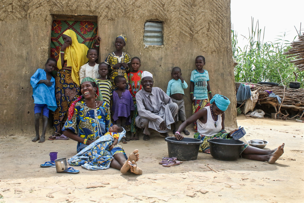 Moussa, sus dos esposas, incluyendo a Absatou, y sus 10 hijos frente a la casa de la familia. Rahila, la segunda esposa, está pelando judías para la comida.