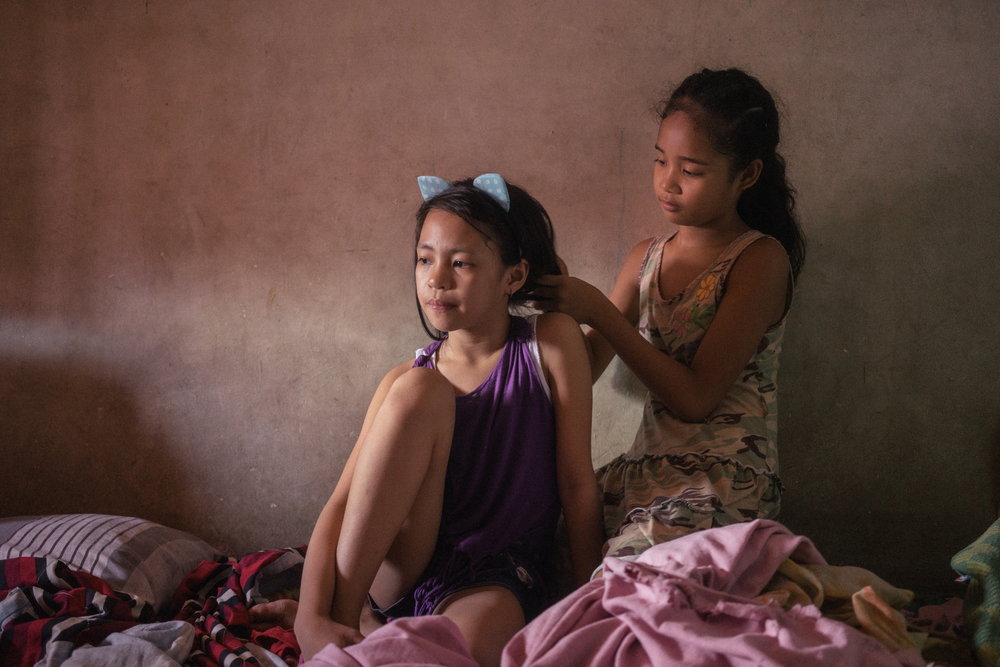 Las jóvenes Elyes y Diana se arreglan el pelo el uno al otro antes de posar para un retrato en su casa de vecinos cerca de Smokey Mountain, Manila. Ambas niñas son beneficiarias de vacunas gratuitas de la clínica de Likhaan, que brinda atención médica 