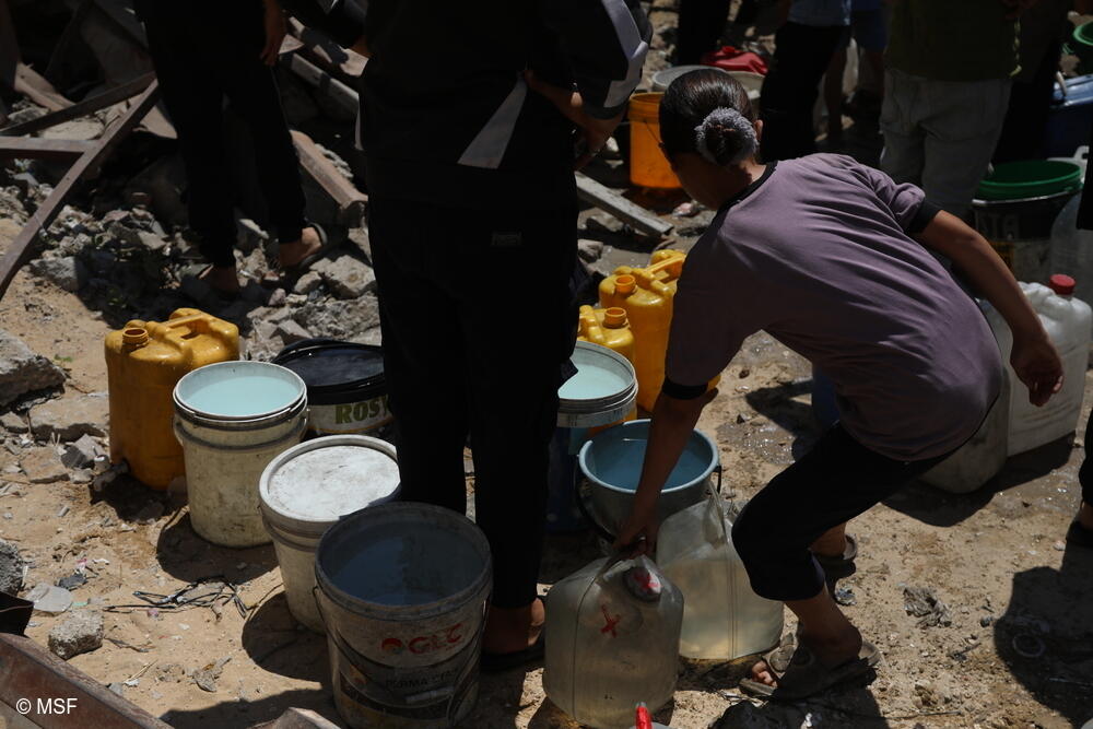 Los palestinos esperan con recipientes gastados para llenarlos desde un camión. La escasez de agua en Gaza y el peligro que supone su recogida crean una tensión enorme.