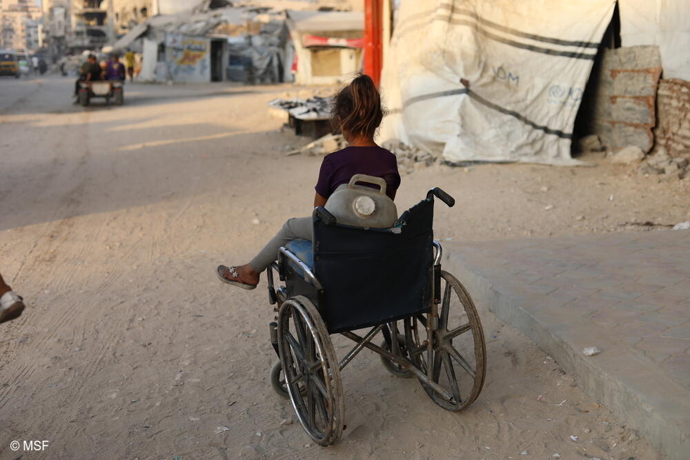 Una niña sentada en una silla de ruedas que utiliza para transportar bidones de agua en Gaza.
