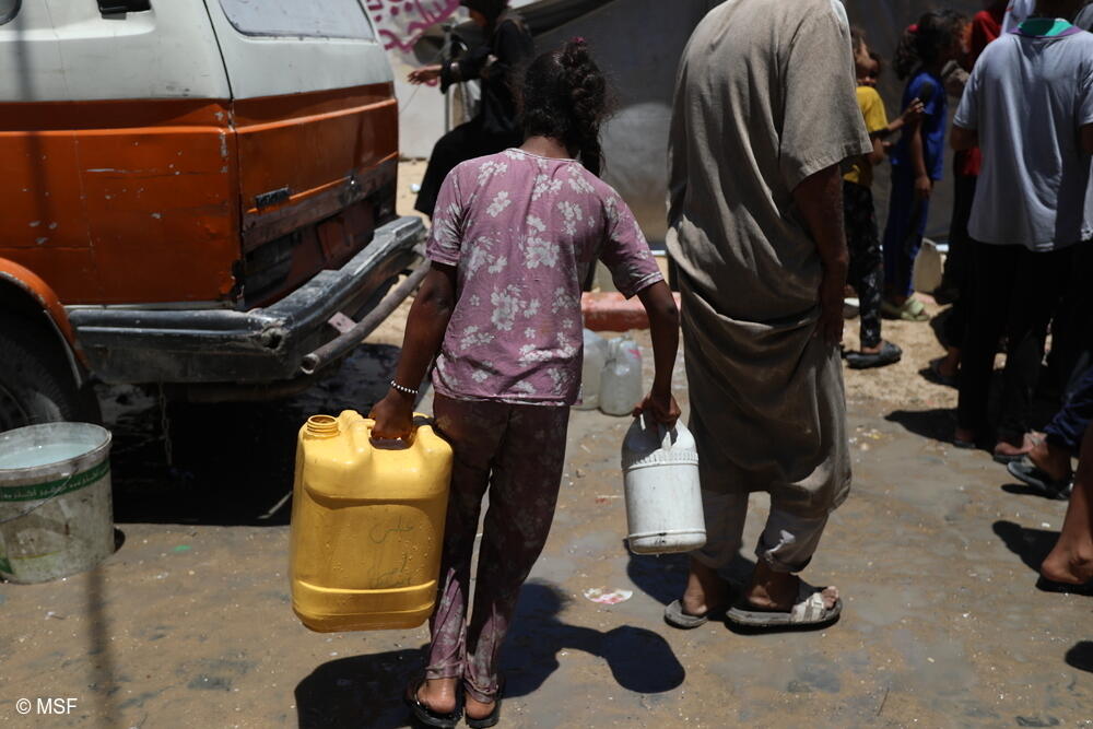 Una niña pequeña lleva un pesado bidón de agua en Gaza, lo que ilustra el colapso total de las infraestructuras públicas.