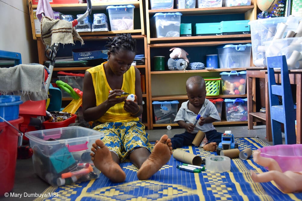 Morrison Williams, de un año, y su mamá, Adama Williams, disfrutan de una sesión de terapia de juego individual en el Hospital Materno-Infantil de MSF. Adama está haciendo un sonajero con arroz y una botella de plástico vacía.
