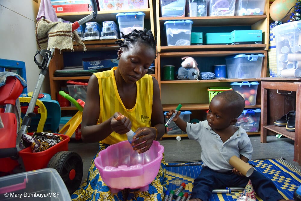 Morrison Williams, de un año, y su mamá, Adama Williams, disfrutan de una sesión de juego individual en el Hospital Materno-Infantil de MSF. Adama está haciendo un sonajero con arroz y una botella de plástico vacía. Adama y Morrison llegaron al hospital en agosto de 2025, después de que Morrison tuviera fiebre alta y le diagnosticaran malaria, lo que le dejó tan débil que no podía caminar.