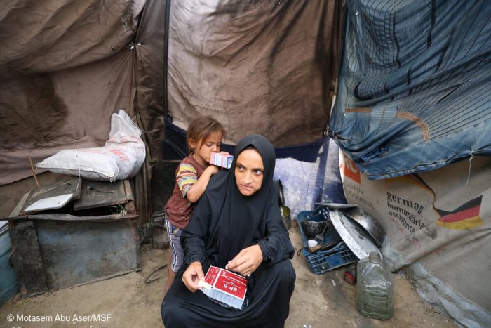 Nour, embarazada de siete meses, come galletas energéticas para combatir la desnutrición mientras su hijo pequeño bebe leche a su lado. La familia vive en una tienda de campaña para desplazados, donde el acceso a alimentos nutritivos es escaso, lo que pone en especial riesgo a las mujeres embarazadas y los niños pequeños.