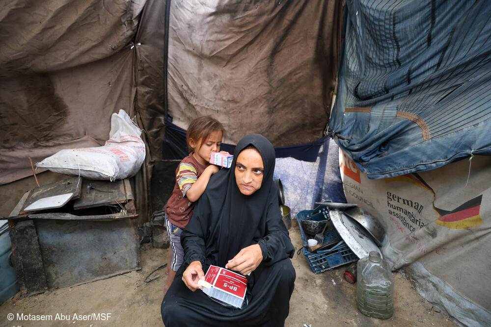 Nour, embarazada de siete meses, come galletas energéticas para combatir la desnutrición mientras su hijo pequeño bebe leche a su lado. La familia vive en una tienda de campaña para desplazados, donde el acceso a alimentos nutritivos es escaso, lo que pone en especial riesgo a las mujeres embarazadas y los niños pequeños.
