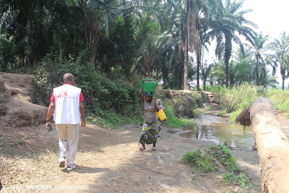 Un técnico de agua, saneamiento e higiene de MSF, durante una visita de supervisión a las instalaciones de cloración del agua, se encuentra con una mujer que acaba de sacar agua del río Luke, en la aldea de Katanga, territorio de Fizi, Kivu del Sur, República Democrática del Congo.