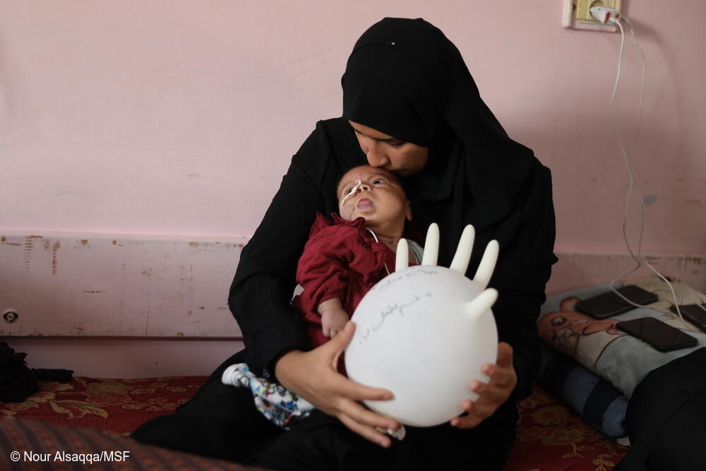 Janna Mtair, de tres meses, yace en el regazo de su madre en el Hospital Nasser tras haber nacido con el síndrome de Beckwith-Wiedemann. Nacida durante el genocidio, su estado empeora al no tener acceso a atención médica especializada a la que podría acceder mediante una evacuación médica.